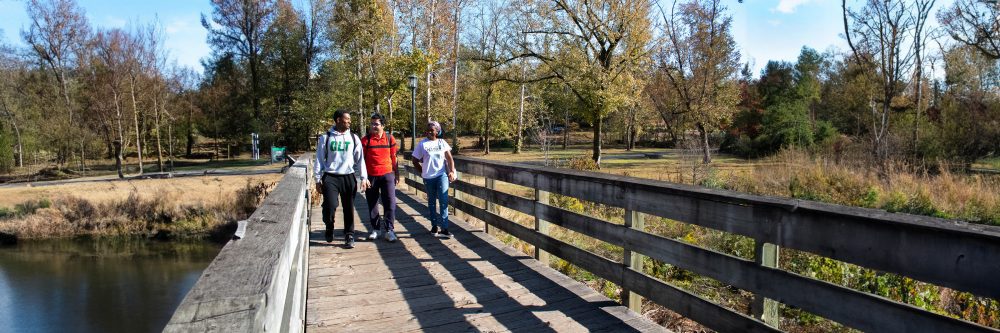 Three students walking across a bridge 